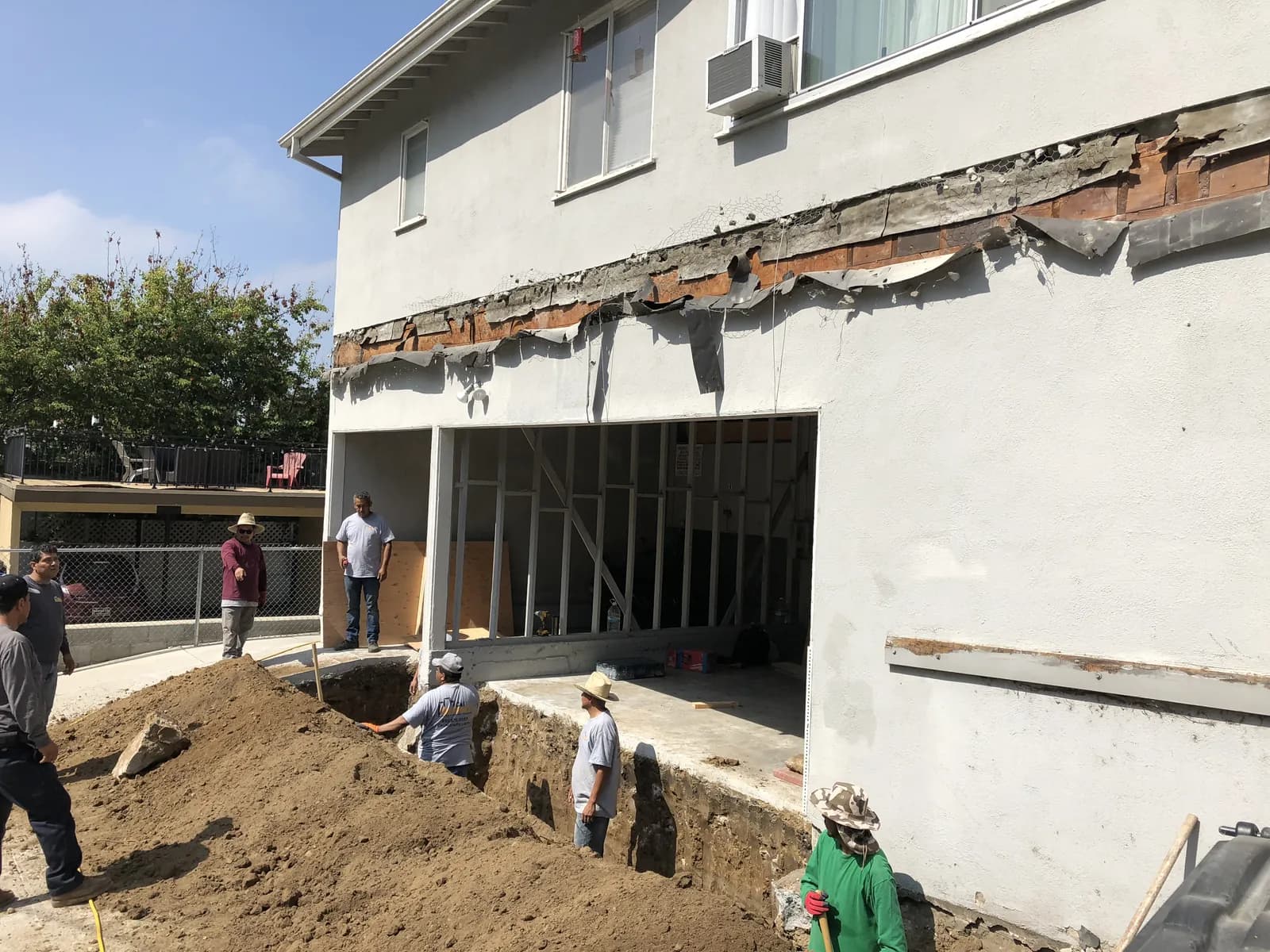 Balcony line demolition and adjacent foundation excavation on a two-story stucco multifamily building.