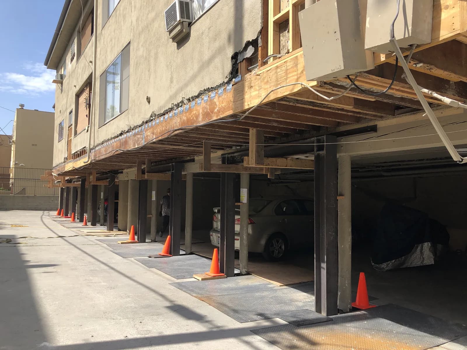 Soft-story apartment building on temporary steel shoring during a seismic retrofit, with ground-floor tenant parking kept in use